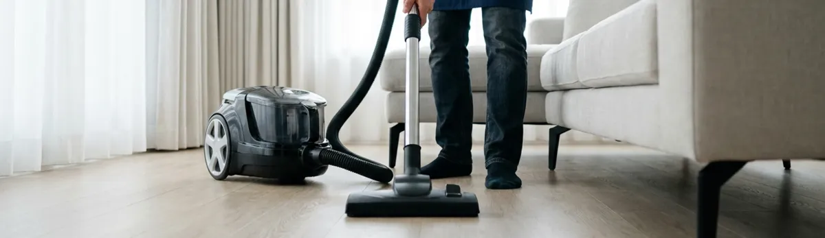 Professional house cleaner vacuuming a living room floor with a canister vacuum cleaner, Akron, OH.