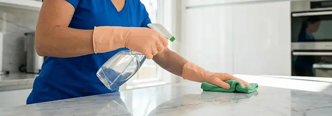 Maid service worker spraying and wiping a kitchen countertop with a microfiber cloth for sanitizing, Akron, OH.