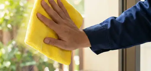 House cleaner wiping a glass window with a yellow microfiber cloth for streak-free cleaning, Akron, OH.